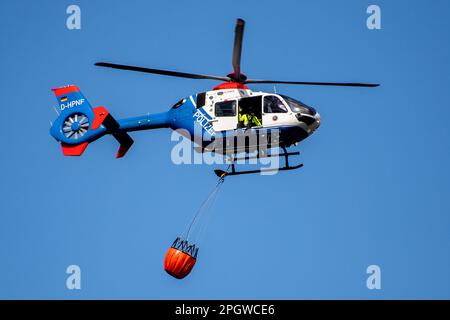 Bad Zwischenahn, Deutschland. 24. März 2023. Ein Phoenix-98-Hubschrauber der niedersächsischen Polizei fliegt über einen Flugplatz mit einem Feuerlöschwassertank, dem sogenannten Bambi-Eimer. Polizeihubschraubergeschwader aus Niedersachsen, Sachsen und Bayern Proben für Notfälle über zwei Tage im Ammerland-Bezirk Niedersachsen. Bis zum 25. März 2023 werden etwa 60 Polizisten und Feuerwehrleute Wälder und Waldbrände aus der Luft bekämpfen. Kredit: Hauke-Christian Dittrich/dpa/Alamy Live News Stockfoto