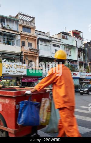 Ho-Chi-Minh-Stadt, Vietnam: Geschäfte und Apartments im Zentrum von Ho-Chi-Minh-Stadt mit einem verwischten Straßenkehrer in orangefarbener Kleidung Stockfoto