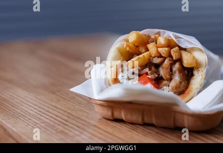 Griechisches Souvlaki-Fleisch, verpackt in Pita-Brot mit Pommes und weißer Tzatziki-Sauce, serviert auf Einweg-Papierteller zum Mitnehmen Stockfoto