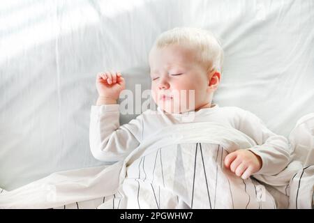 Ein kleines Baby schläft süß auf einem weißen Laken im Kinderzimmer. Glückliche Kindheit und Schlafprobleme bei Kindern Konzept. Stockfoto