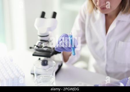 Eine Mitarbeiterin untersucht die Probe im Reagenzglas mit einem Mikroskop Stockfoto