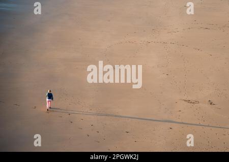 Nicht erkannte Person, die bei Sonnenuntergang am Sandstrand spaziert. Gesunder Lebensstil. Sport im Freien Stockfoto