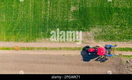 Über der Draufsicht des Traktors als Ziehen eines montierten Setzgrubber, einer Egge und Fahren auf schmutzigen Straßen, zwischen bebauten Feldern. Stockfoto