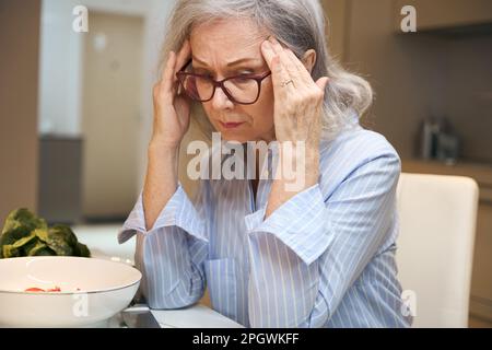 Die einsame ältere Dame sitzt am Küchentisch Stockfoto