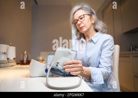 Ältere, müde Frau verwendet ein Tonometer zur Blutdrucküberwachung Stockfoto