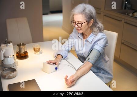 Einsame Rentnerin misst ihren Blutdruck mit einem modernen Tonometer Stockfoto