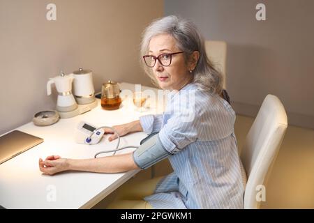 Eine ältere Dame misst ihren Blutdruck mit einem Tonometer Stockfoto