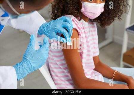 Der Arzt hält die Spritze fest und desinfiziert sie an der Hand des Kindes, bevor der Impfstoff injiziert wird. Stockfoto