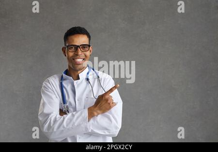 Freundlich lächelnder männlicher afroamerikanischer Arzt zeigt mit dem Finger beiseite Stockfoto