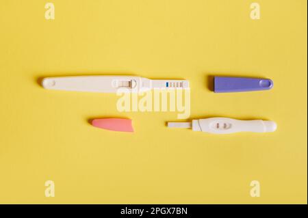 Flache Auflage von zwei Trächtigkeits-Inkjet-Testsätzen mit zwei Streifen – positives Ergebnis auf gelbem Hintergrund. Endlich schwanger Stockfoto