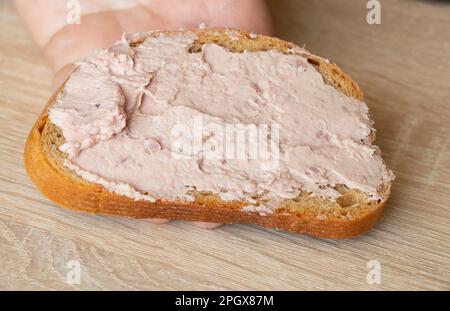 Die Hand eines Mannes hält ein Sandwich mit einer Paste Stockfoto