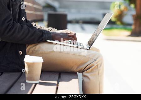 Arbeiten mit einem Laptop. Nahaufnahme eines afroamerikanischen Mannes in schwarzer Jacke im Freien in der Stadt, der auf einer Bank sitzt Stockfoto