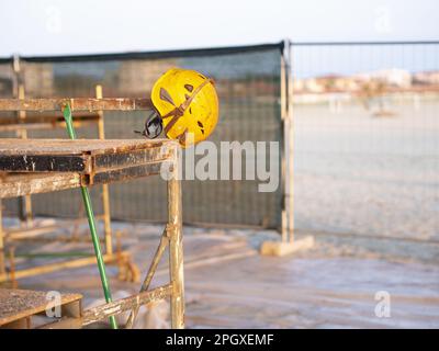 Helm und Schutzbrille (Beispiel für persönliche Schutzausrüstung zur Verbesserung der Sicherheit am Arbeitsplatz), die auf einem Gerüst auf einer Baustelle ruht Stockfoto