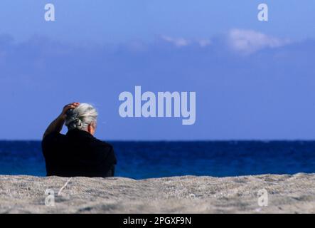 Alte Dorffrau am Meer. Marina di Orosei, der Strand an der Mündung des Flusses Cedrino. Orosei (Nuoro) Sardinien. Italien. Stockfoto