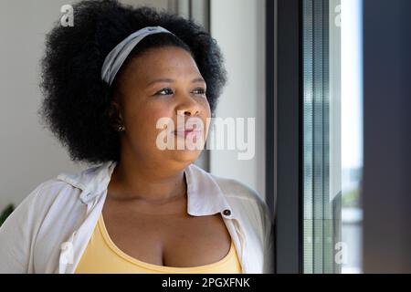 Eine fürsorgliche afroamerikanerin in Übergröße, die aus dem Fenster schaut Stockfoto