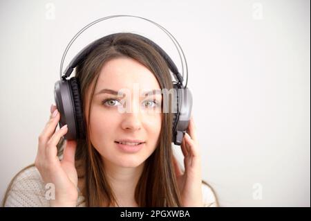 Panoramafilter-Nahaufnahme einer wunderschönen jungen Frau mit elegantem, lässigem Outfit isoliert über einer farbenfrohen Hintergrundwand, mit weißen, kabellosen Kopfhörern und Musik hören und benutzen Stockfoto