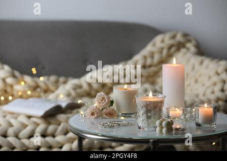 Brennende Kerzen, Blumen und Schmuck auf dem Tisch im Zimmer Stockfoto