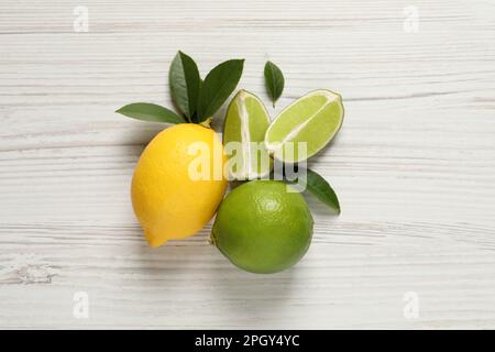 Frische, reife Zitrone, Limetten und grüne Blätter auf weißem Holzhintergrund, flach liegend Stockfoto