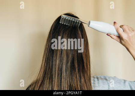 Frau benutzt Darsonval zur Massage der Kopfhaut. Elektrische Darsonvalmassage im Gesicht. Hochwertiges Foto Stockfoto