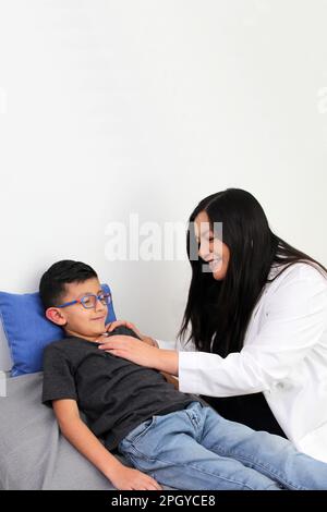 Latina Kinderärztin untersucht ihren 6-jährigen Jungen auf Halsschmerzen durch Mandelentzündung oder Pharyngitis, die Husten verursachen Stockfoto