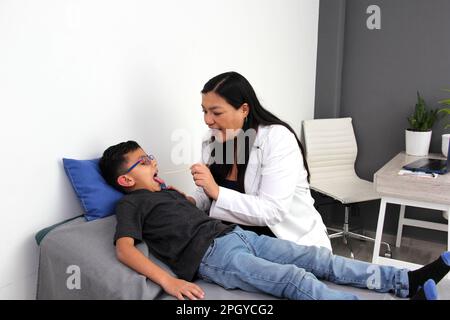 Latina Kinderärztin untersucht ihren 6-jährigen Jungen auf Halsschmerzen durch Mandelentzündung oder Pharyngitis, die Husten verursachen Stockfoto