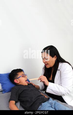 Latina Kinderärztin untersucht ihren 6-jährigen Jungen auf Halsschmerzen durch Mandelentzündung oder Pharyngitis, die Husten verursachen Stockfoto