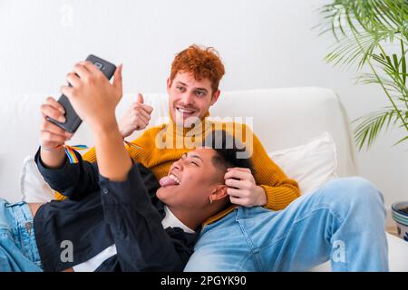 Ein wunderschönes schwules Paar, das im Haus romantisch auf dem Sofa ist, ein schwules Paar, das ein Selfie macht Stockfoto