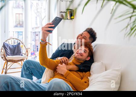 Wunderschönes schwules Paar, das zu Hause auf dem Sofa romantisch ist, ein Selfie macht, lgbt-Konzept Stockfoto