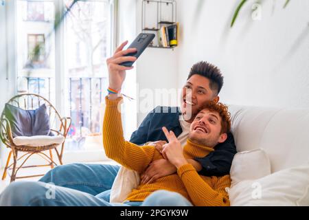 Wunderschönes schwules Paar, das zu Hause auf dem Sofa romantisch ist, während eines Videogesprächs, lgbt-Konzept Stockfoto