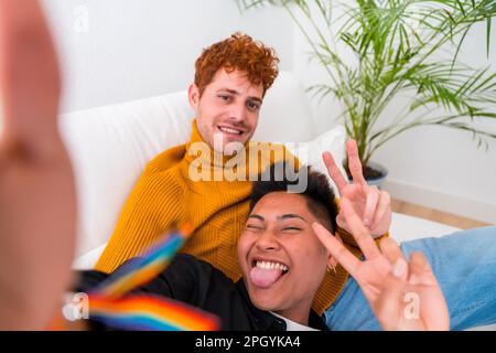 Wunderschönes schwules Paar, das zu Hause romantisch ist, auf dem Sofa, schwules Paar, das Selfie macht und Siegeszeichen macht, lgbt-Konzept Stockfoto