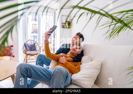 Wunderschönes schwules Paar, das zu Hause auf dem Sofa romantisch ist, ein Selfie macht, lgbt-Konzept Stockfoto