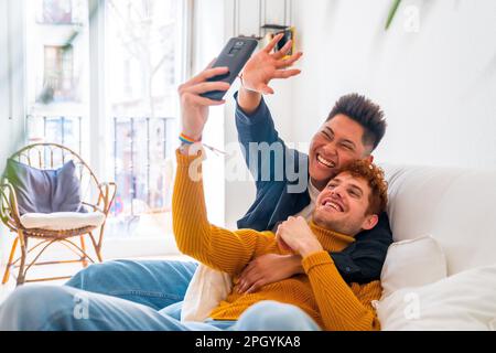 Wunderschönes schwules Paar, das zu Hause auf dem Sofa romantisch ist, während eines Videogesprächs, lgbt-Konzept Stockfoto