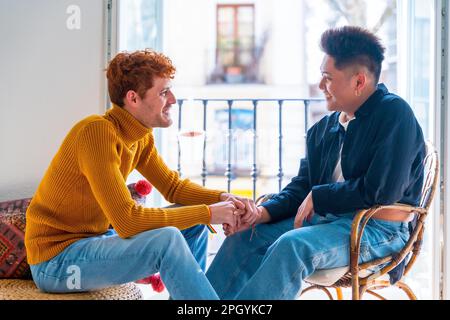 Wunderschönes schwules Paar, das zu Hause am Balkon romantisch ist und sich die Hände schüttelt, lgbt-Konzept Stockfoto