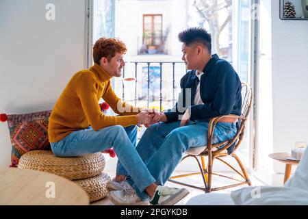 Wunderschönes schwules Paar, das zu Hause am Balkon romantisch ist und sich die Hände schüttelt, lgbt-Konzept Stockfoto