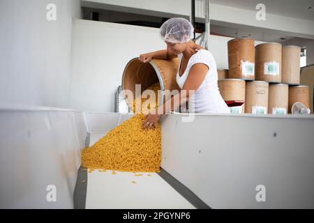 Frau mit Haarschutz, die Nudeln aus einem Staufach in eine Wanne kippt, Finkensteiner Nudelfabrik, Finkenstein am Faaker See, Region Villach Stockfoto