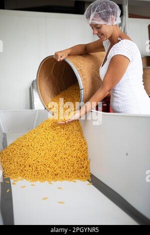 Frau mit Haarschutz, die Nudeln aus einem Staufach in eine Wanne kippt, Finkensteiner Nudelfabrik, Finkenstein am Faaker See, Region Villach Stockfoto