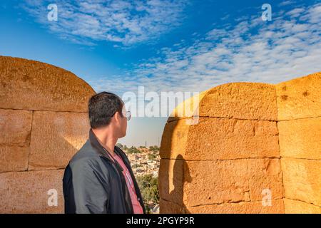 Mann, der tagsüber die architektonische Aussicht auf die Wüstenstadt mit hellblauem Himmel von der Festung jaisalmer aus beobachtet Stockfoto