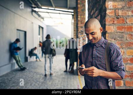 Sein Semesterplan ist digitalisiert. Ein junger Mann, der draußen auf dem Campus ein Handy benutzt. Stockfoto