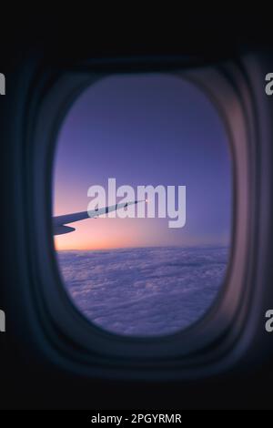 Blick aus dem Fenster des Flugzeugs während des Fluges über den Wolken bei Sonnenaufgang. Selektiver Schwerpunkt auf Flugzeugflügel. Stockfoto