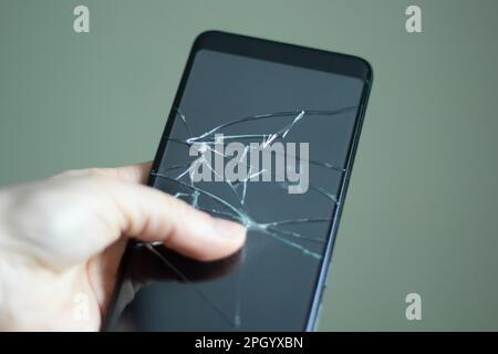 Schwarzes Touchscreen-Telefon mit einem kaputten Bildschirm in der Hand des Mädchens Nahaufnahme Stockfoto