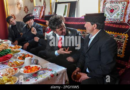 (230325) -- TAXKORGAN, 25. März 2023 (Xinhua) -- Duri Jarman (1. R) spricht mit Freunden in seinem Haus in Aimin Village des Taxkorgan Tajik Autonomous County, Nordwestchina Xinjiang Uygur Autonomous Region, 21. März 2023. Das Leben des Hirten Duri Jarman ist eng mit zwei Orten verbunden: Dem Dorf AK Toga Langar, eingebettet tief in die Berge des Taxkorgan Tajik Autonomous County, und dem Dorf Aimin, das sich in der Nähe des Bezirkssitzes befindet. Duri, jetzt 52 Jahre alt, lebte 47 Jahre im Dorf AK Toga Langar. Im Winter 2018 profitierte seine Familie von der Umsiedlungspolitik für Armutsallee Stockfoto