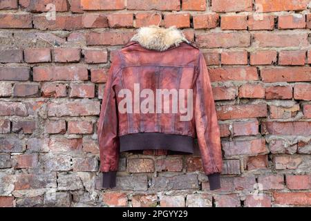 Rotes Pelzleder Winterjacke für Damen hängt tagsüber an einem Kleiderbügel an einer alten Backsteinwand im Freien, Damenbekleidung Stockfoto