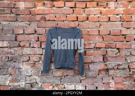 Dunkelblaue Jacke, die an einem Kleiderbügel an einer alten Backsteinmauer in der Straße hängt Stockfoto