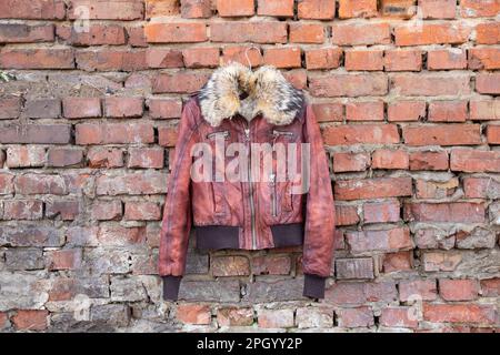 Rotes Pelzleder Winterjacke für Damen hängt tagsüber an einem Kleiderbügel an einer alten Backsteinwand im Freien, Damenbekleidung