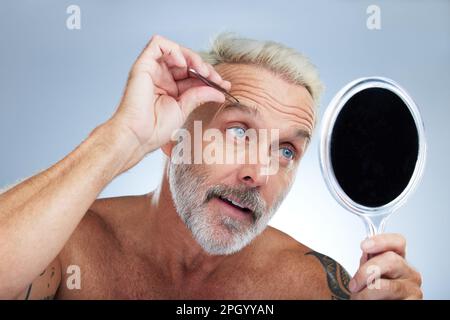 Seniorin, Pinzette und Augenbraue im Studio mit Spiegel, Pflege und Eigenpflege für Schönheit im Hintergrund. Model, Check und Pinzette für Gesichtshaar Stockfoto