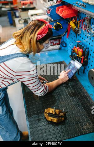 Mechanikerin prüft Scheibenbremse mit Diagnose-App im digitalen Tablet Stockfoto