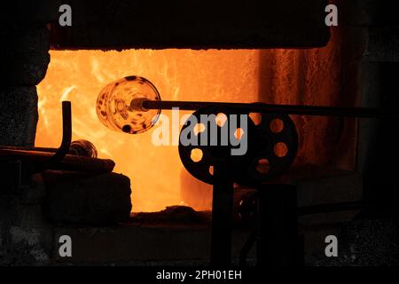 Eine Glasflasche, die in einem Glasschmelzofen erhitzt wird, damit sie manipuliert werden kann. Stockfoto