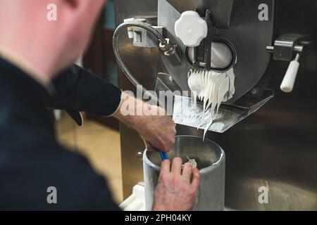 Ein Koch, der weißes Eis aus der Eiscreme-Maschine in der kleinen Produktion bekommt. Hochwertiges Foto Stockfoto