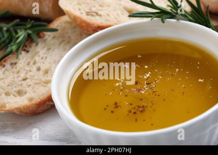 Schüssel mit frischem Öl, Brot und Rosmarin auf weißem Holztisch, Nahaufnahme Stockfoto