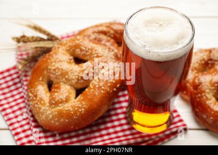 Ein Glas Bier und leckere frisch gebackene Brezeln auf einem weißen Holztisch, Nahaufnahme Stockfoto